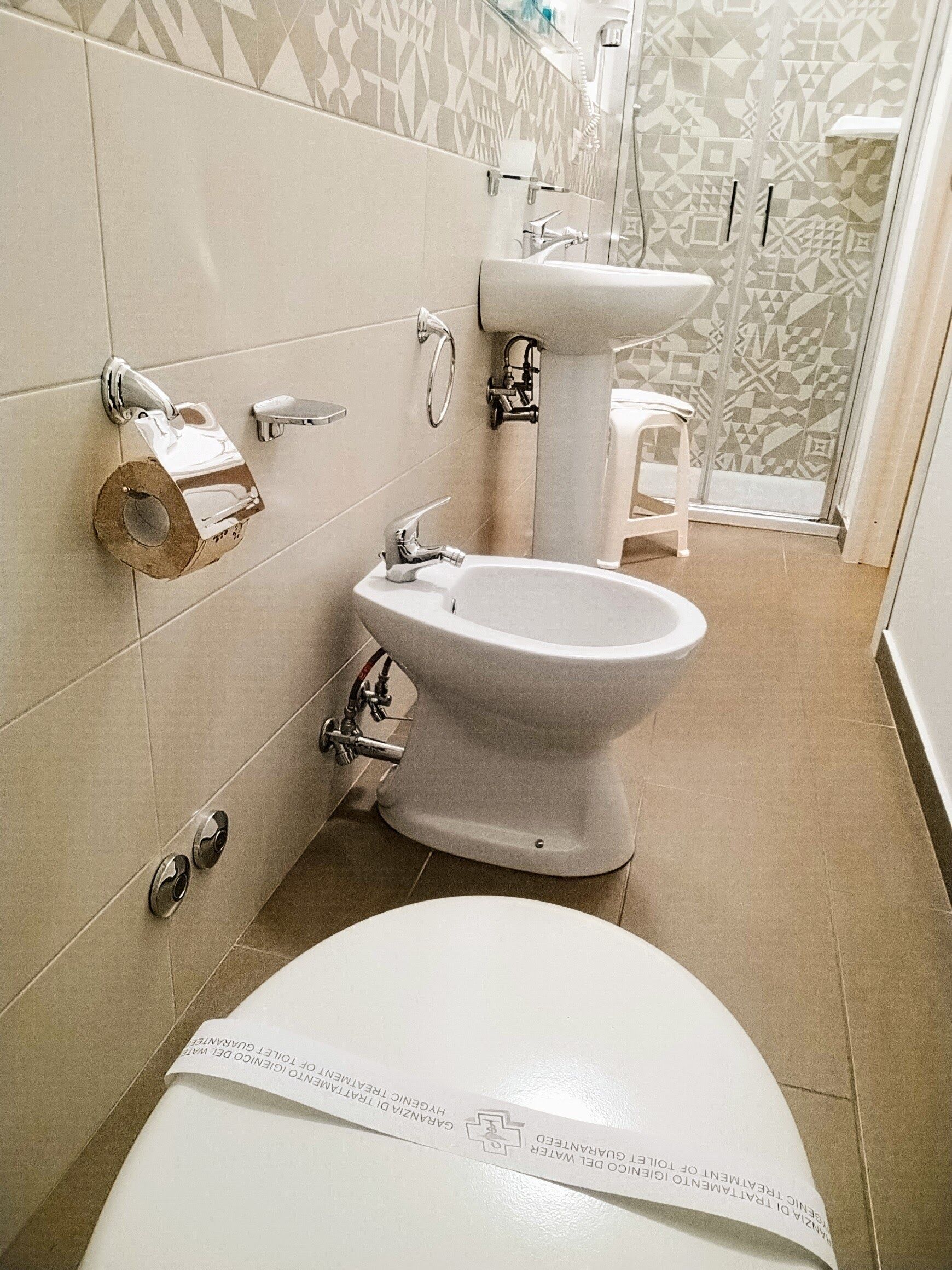 A bathroom with a toilet, bidet, and a small white stool.