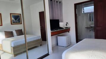 A hotel room with two beds, a desk with a computer, a small refrigerator, and a bathroom with a sink and mirror.