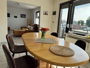Ein Essbereich mit Holztisch, Stühlen, einer Vase mit Blumen und Blick auf die Stadt durch große Fenster.