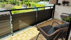 Een balkon met uitzicht op een tuin, een rieten stoel en een bijzettafeltje met een plant.