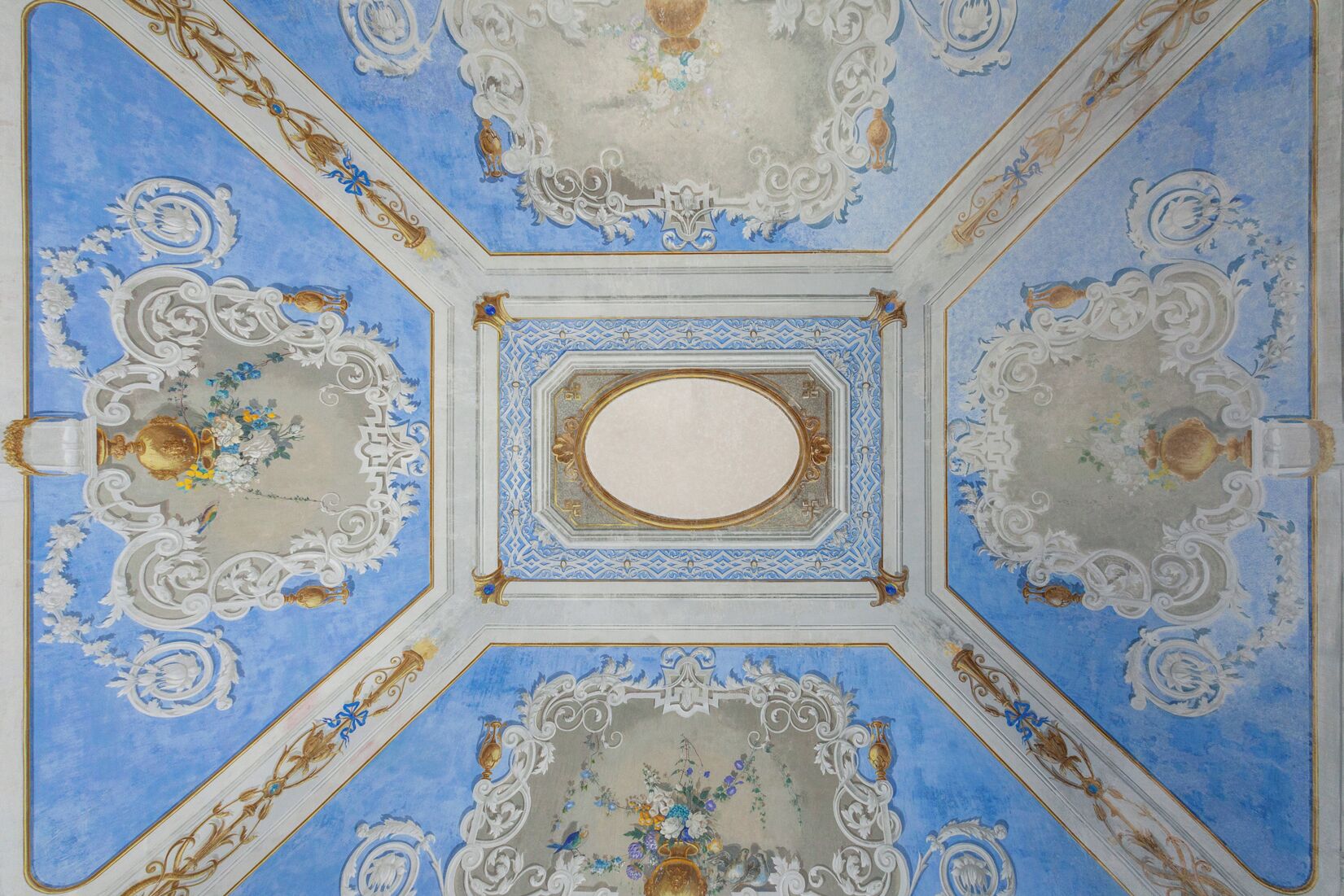 Teto com padrões intrincados em azul e branco, detalhes dourados e um espelho oval central.