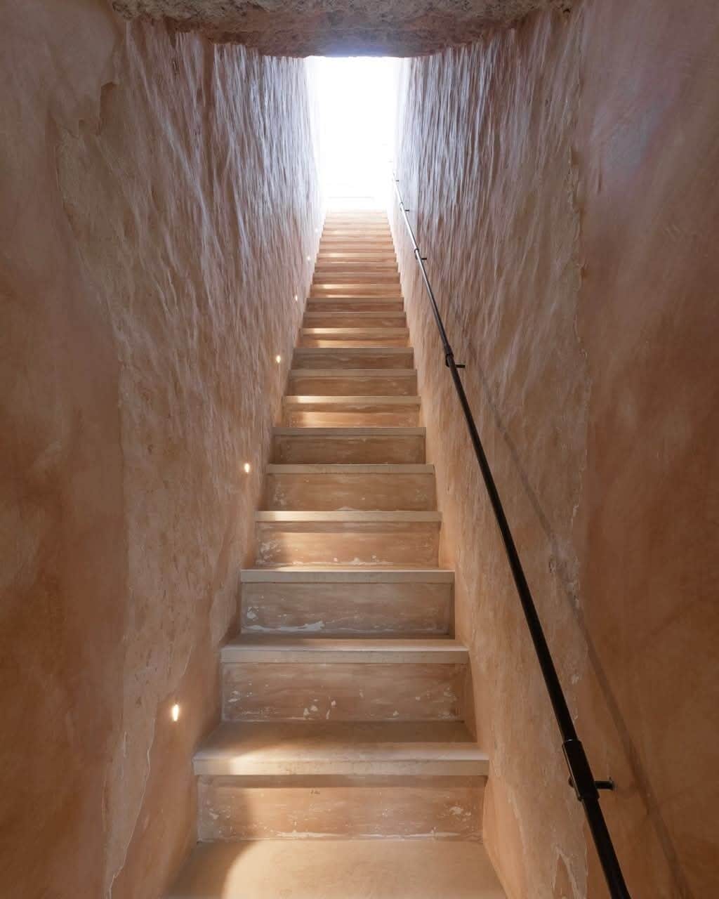 A narrow stairway with a handrail, leading upwards to a bright exit.