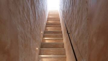 A narrow stairway with a handrail, leading upwards to a bright exit.