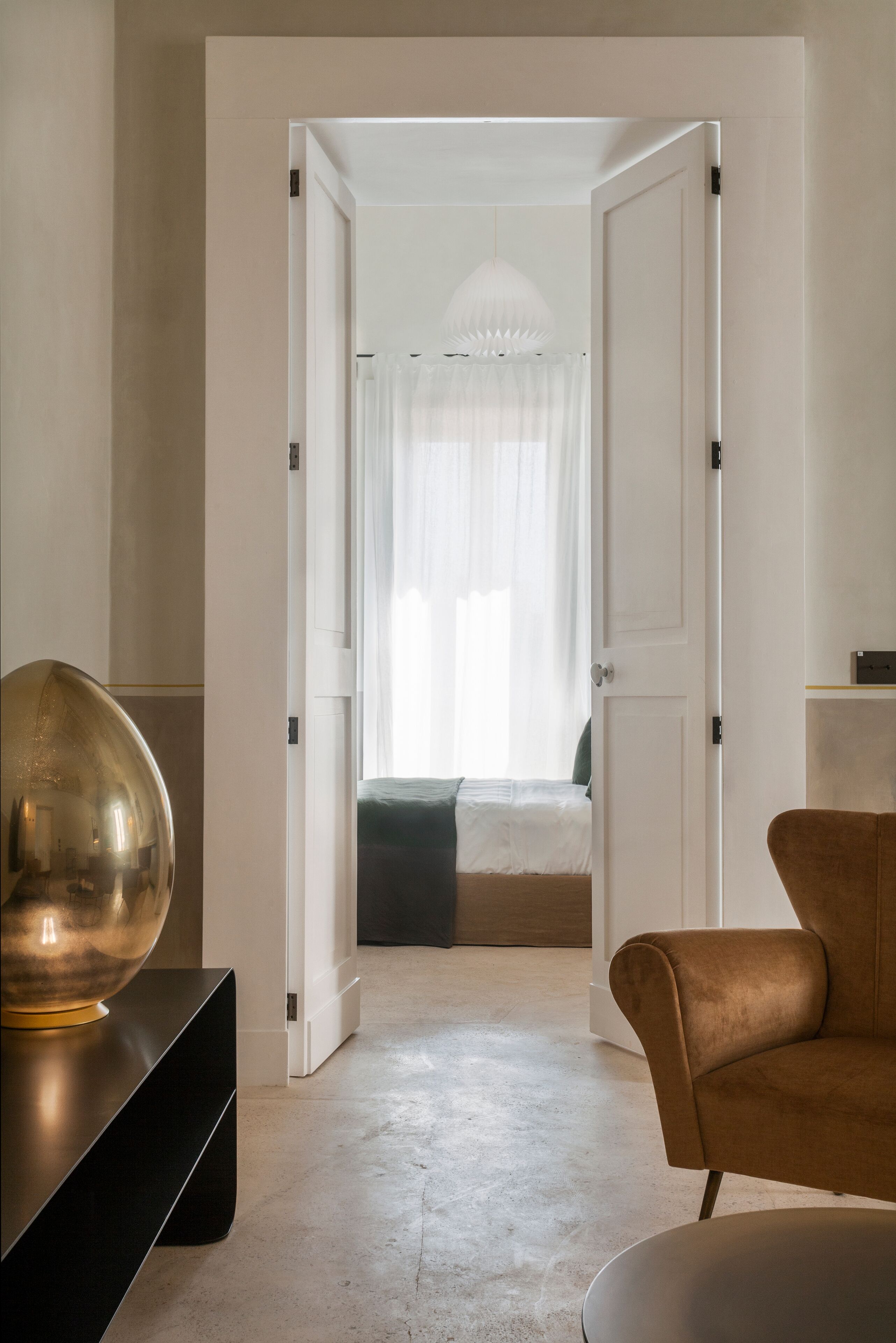 Een moderne hotelkamer met een minimalistisch design, met een grote spiegel, een comfortabele fauteuil en een netjes opgemaakt bed.