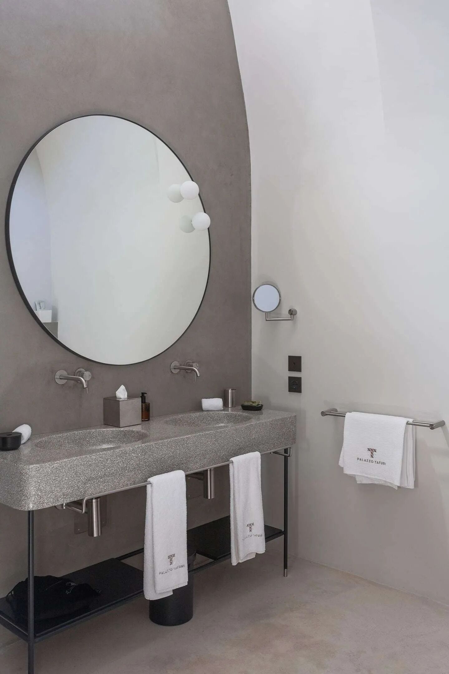 A modern bathroom with a large round mirror, two sinks, and a towel rack.