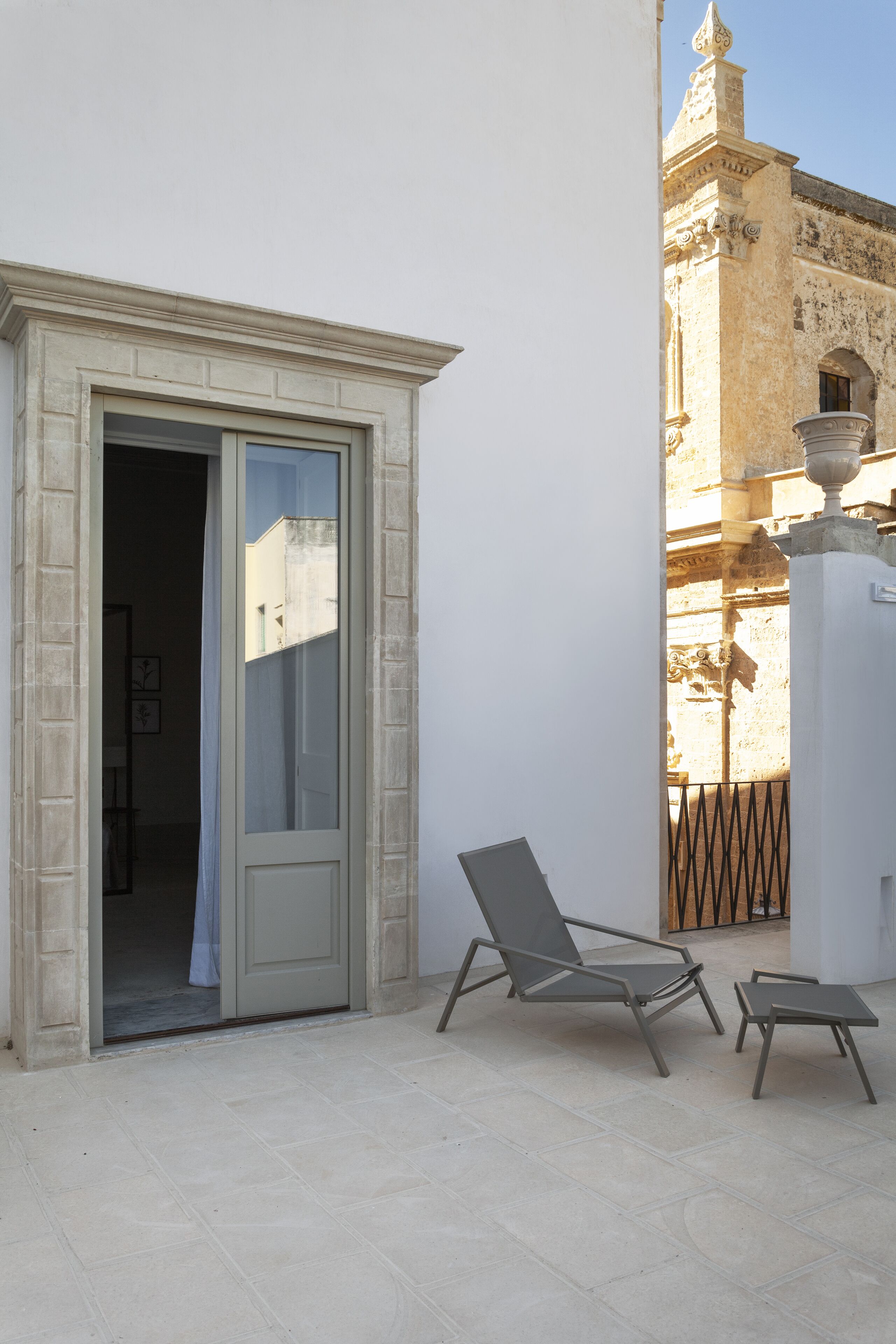 Un balcone con una porta che dà su uno spazio interno, una sedia e un tavolino.