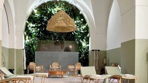 Un área junto a la piscina con sillones de descanso, una mesita pequeña y una lámpara colgante de mimbre.
