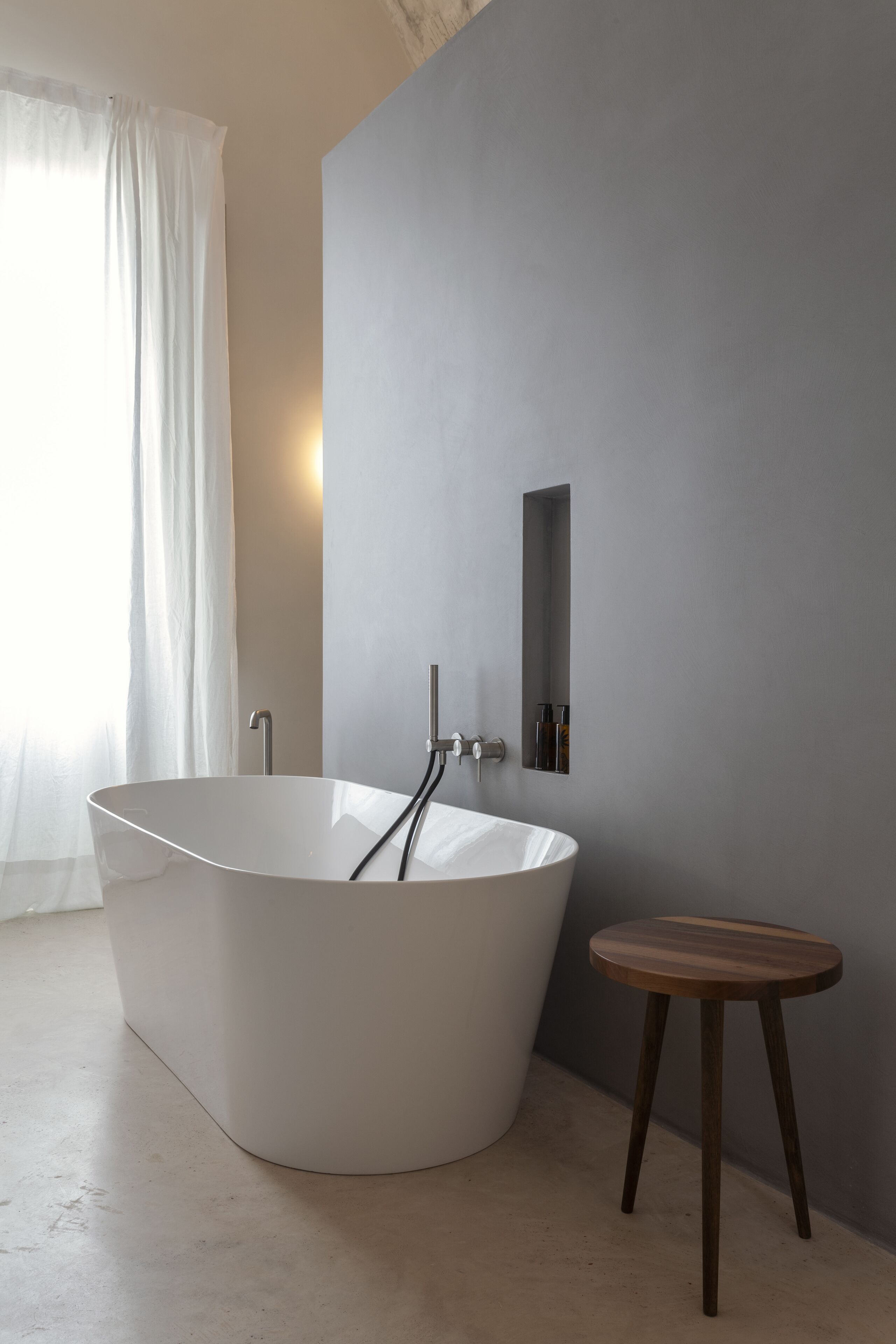 A modern bathroom with a freestanding bathtub, a small wooden stool, and a wall-mounted medicine cabinet.