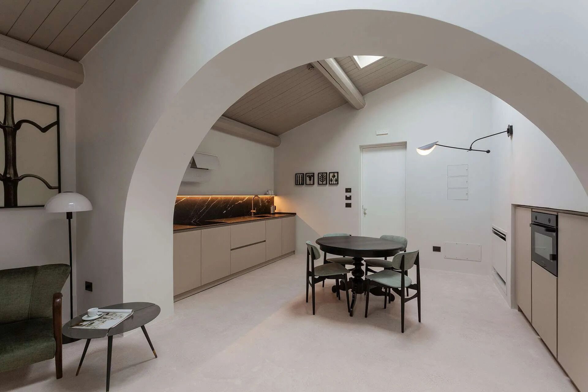 A modern kitchen with an archway leading to a dining area, featuring a marble countertop, white cabinets, and a dining table with chairs.