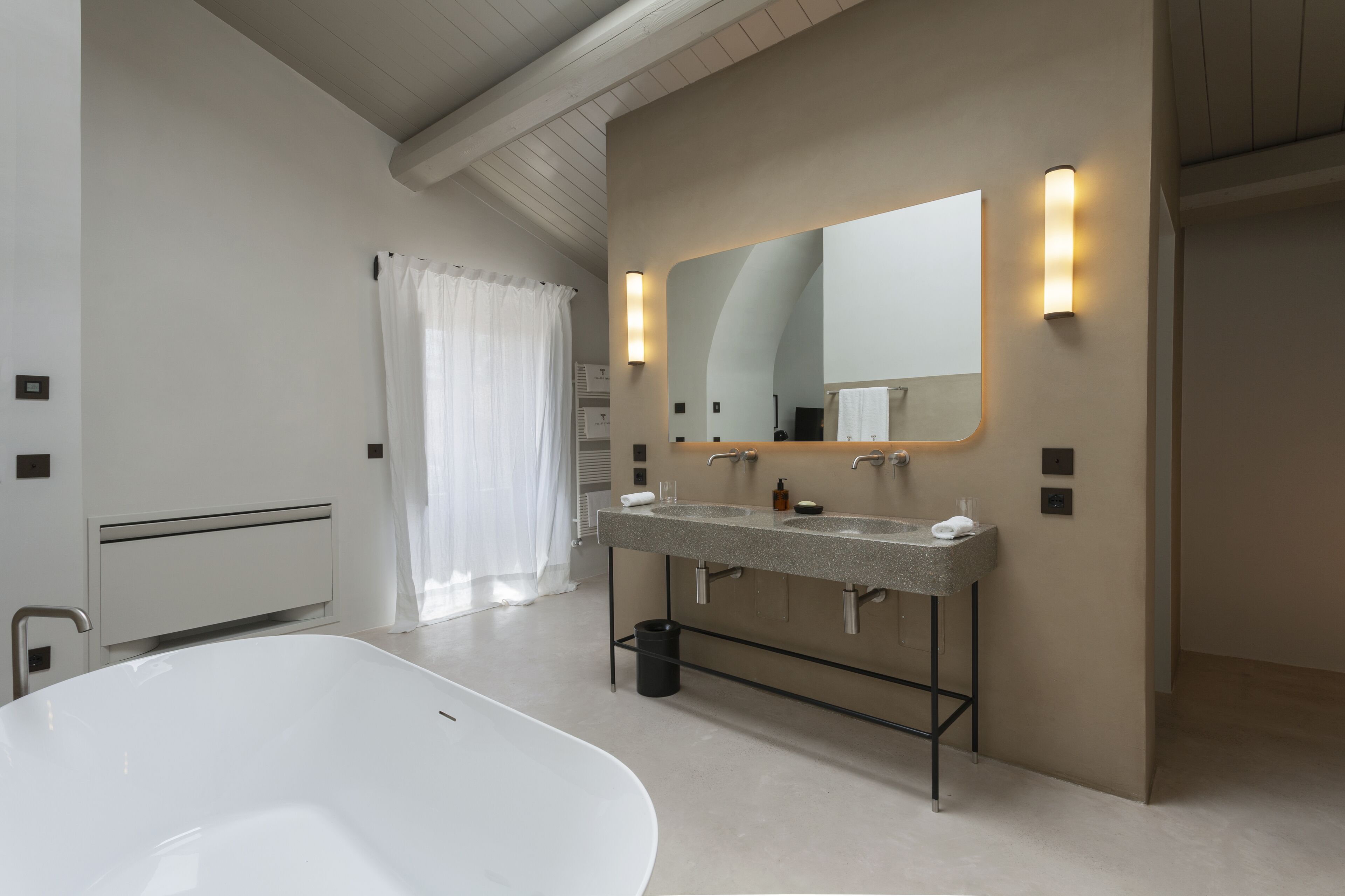 A modern bathroom with a large white bathtub, a double sink vanity, a large mirror, and a light fixture above the mirror.