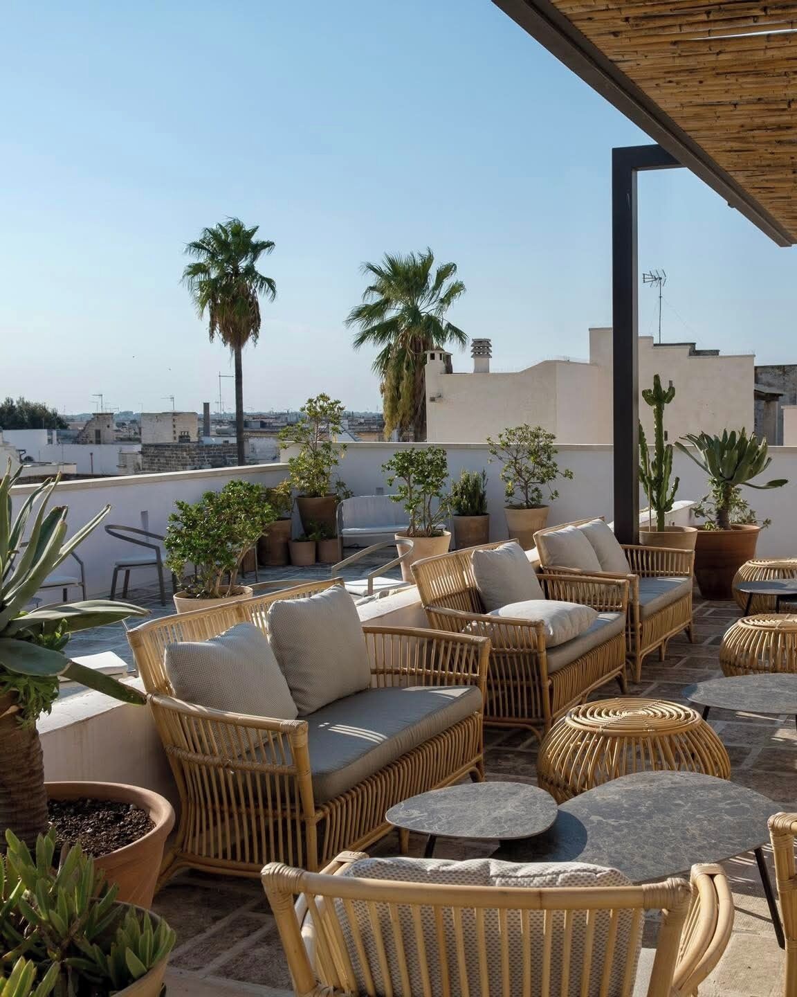 A rooftop terrace with wicker furniture, potted plants, and a view of the cityscape.