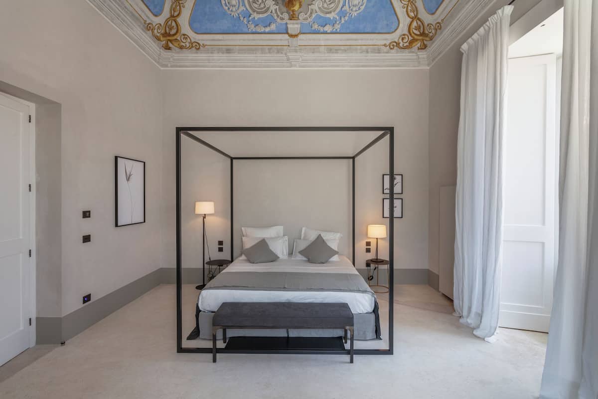 Un dormitorio moderno con cama con dosel, lámparas de noche y un banco.