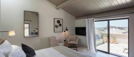 Habitación de hotel con una cama grande, una silla, una mesita, un televisor y un balcón con plantas en macetas.