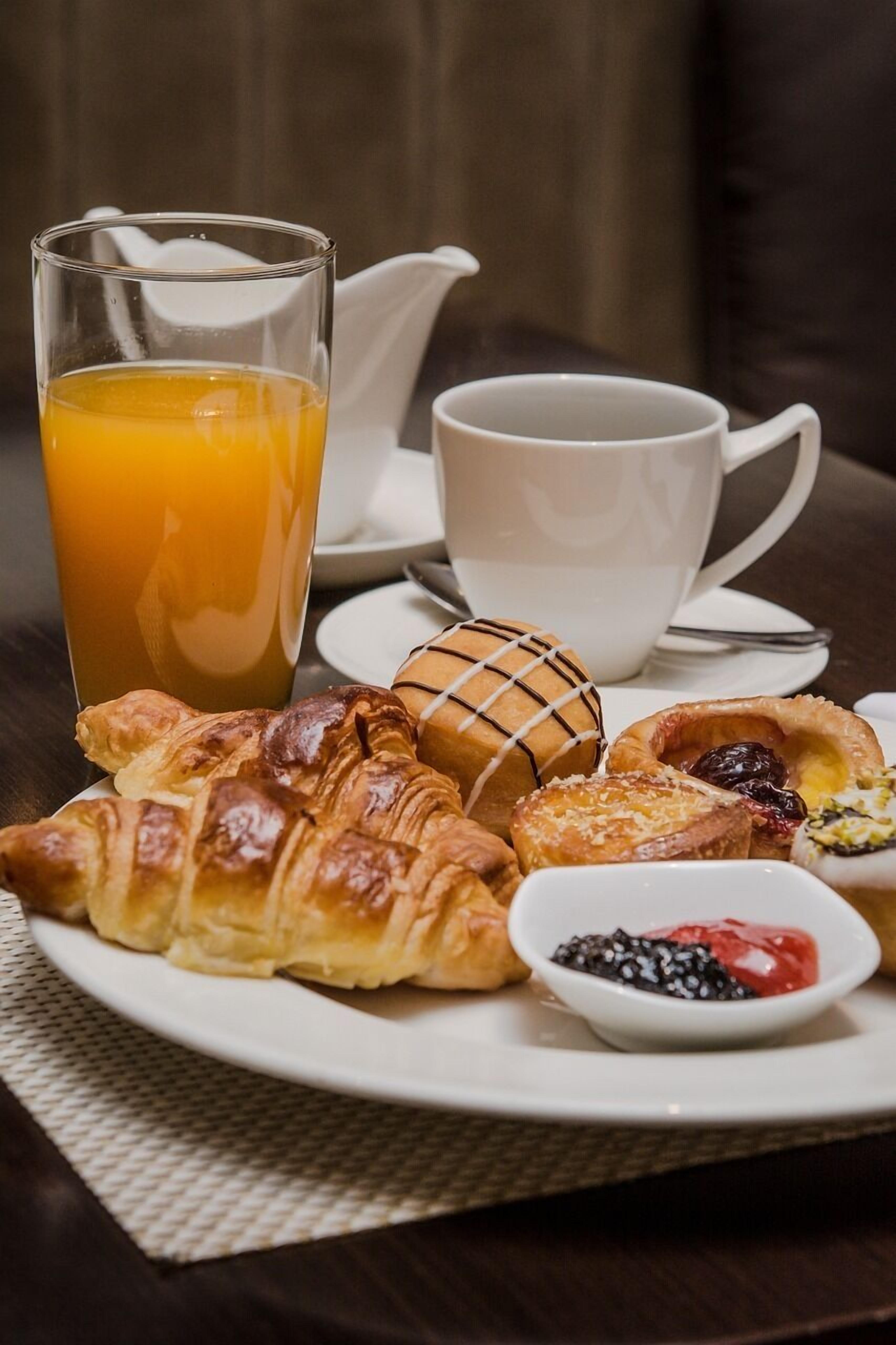 A breakfast setting with croissants, a glass of orange juice, a cup of coffee, and a small bowl of berries on a plate.
