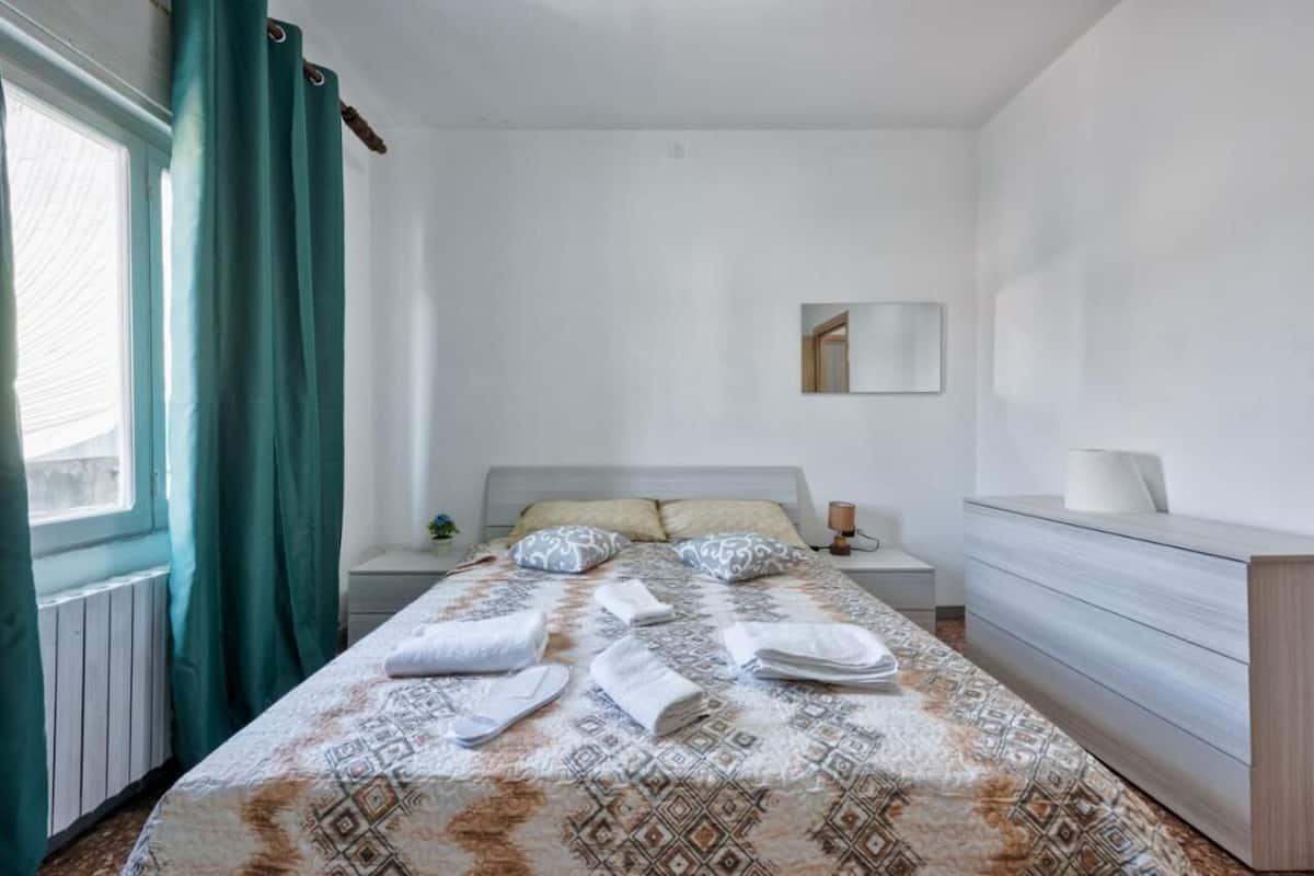A hotel room with a bed, a nightstand, a dresser, and a window with curtains.