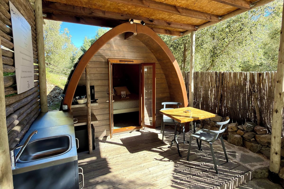 A covered outdoor area with a grill, table, and chairs, and an open door leading to a bedroom.