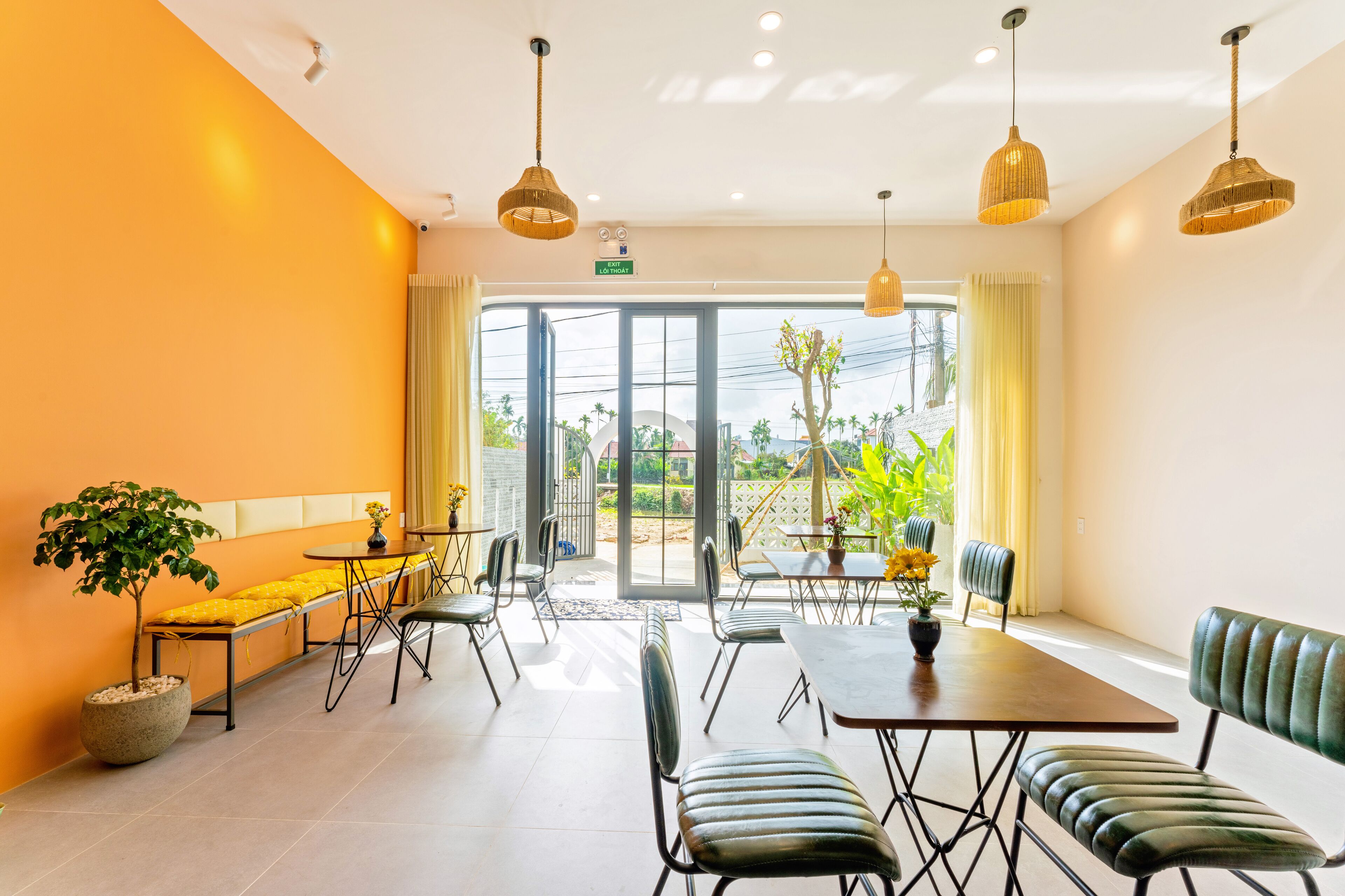 Uma sala de jantar luminosa e moderna, com uma grande janela, várias mesas e cadeiras, e luminárias pendentes.
