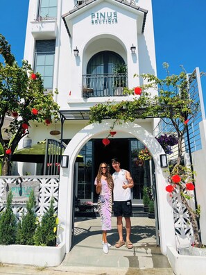 A boutique hotel entrance with a white facade, arched doorway, and a balcony with plants. - Hoi An Pinus Boutique (Da Nang)