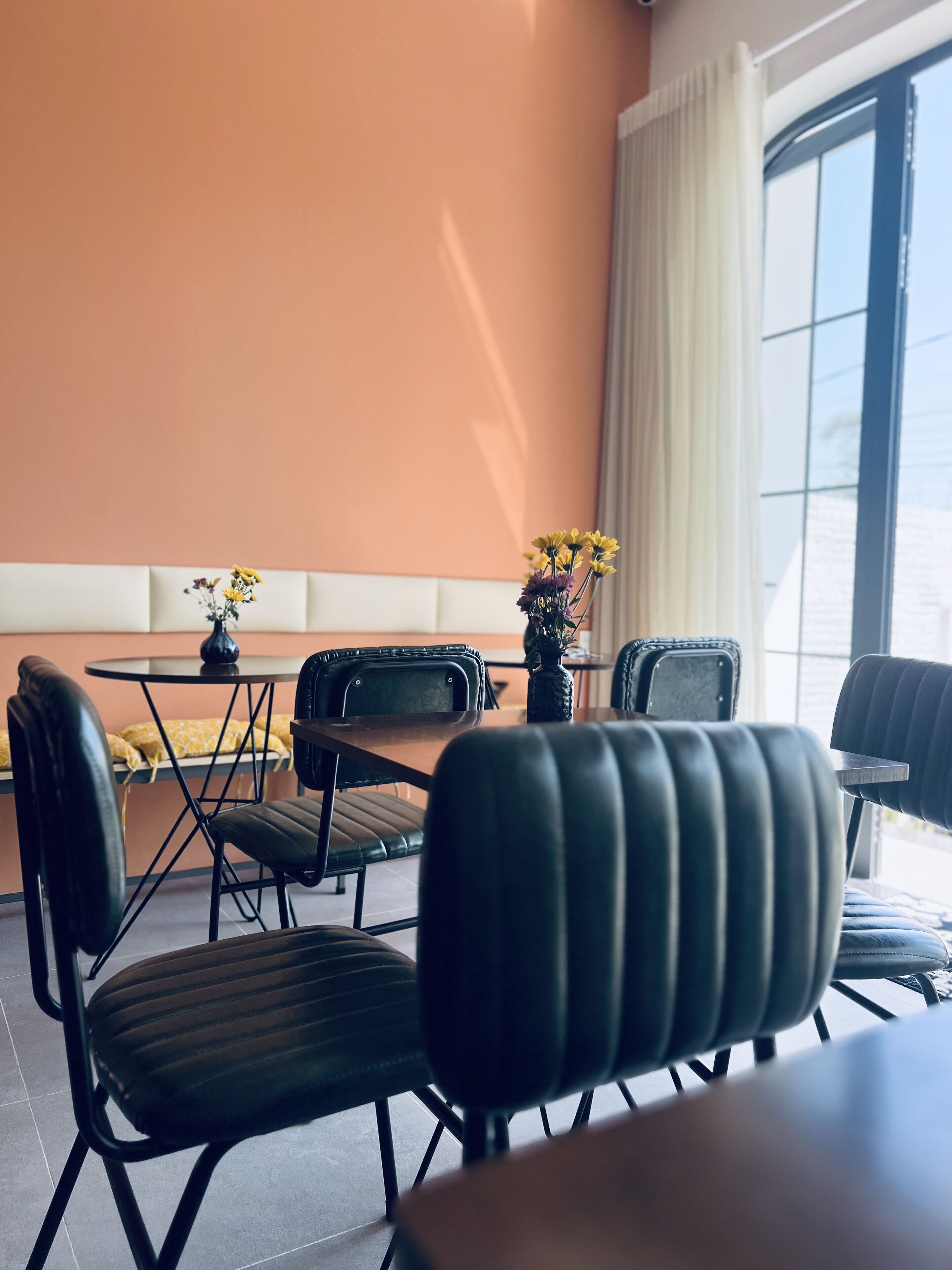 A dining area with a round table, black chairs, and a vase with yellow flowers.