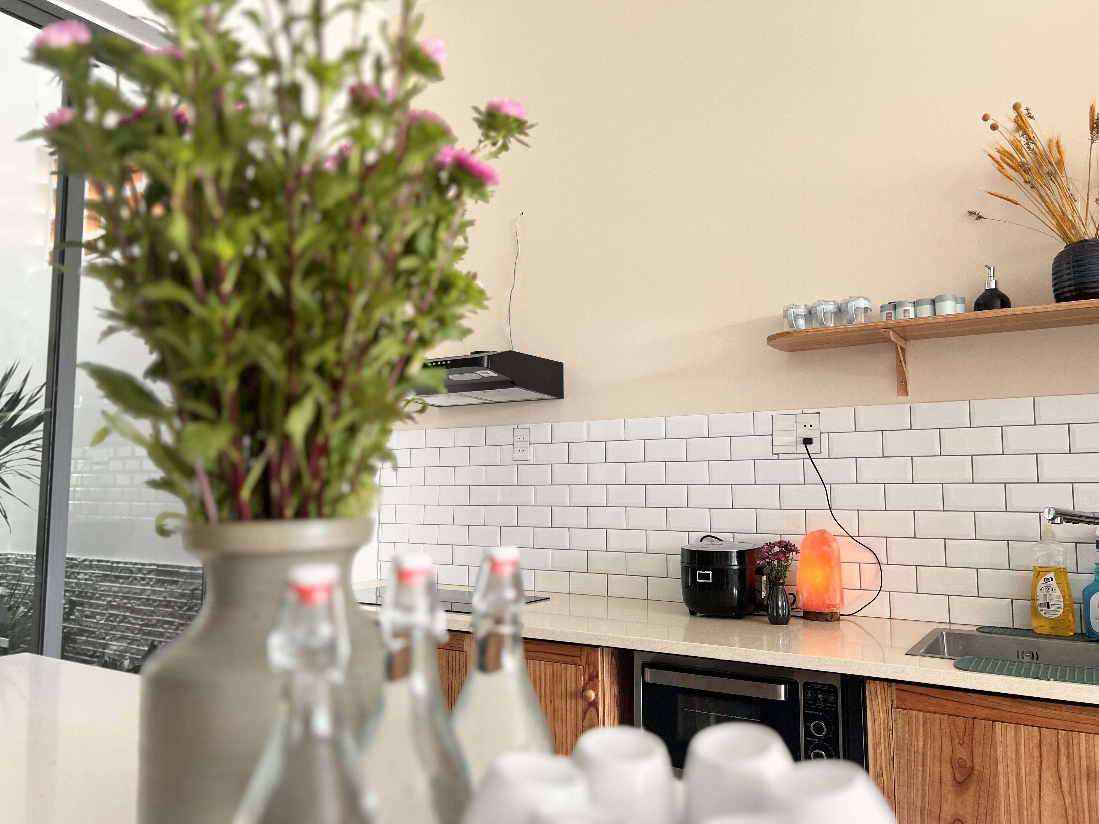 Une cuisine avec un dosseret de carrelage blanc, des armoires en bois, un égouttoir et un vase rempli de fleurs.