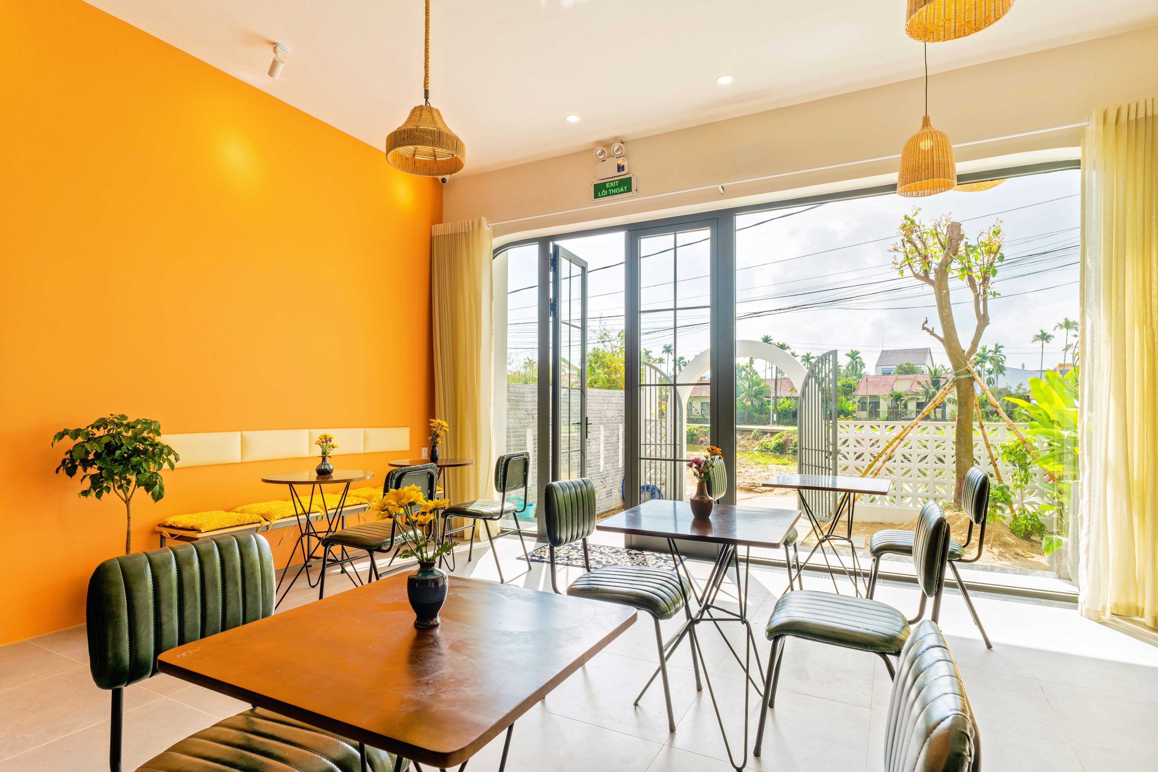 A bright dining area with orange walls, large windows, and a view of the outdoors.