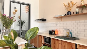 Una cocina moderna con armarios de madera, horno empotrado, microondas y un lavamanos con felpudo verde. Hay plantas en macetas y un jarrón con flores sobre la encimera.