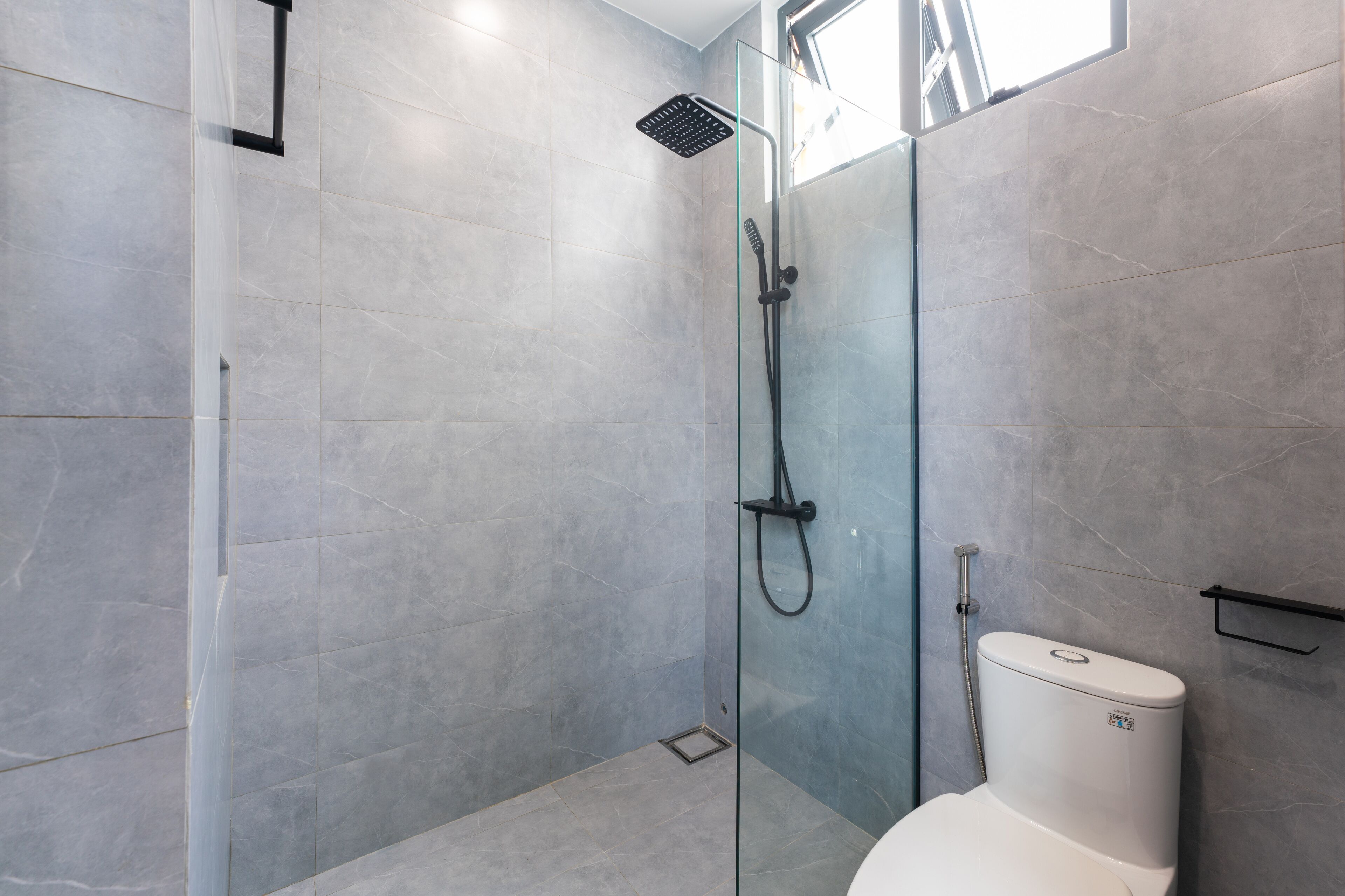 A modern bathroom with a glass-enclosed shower, a toilet, and a small shelf.