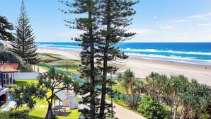 A coastal view with a beach, a clear sky, and a pathway leading to a building with a green roof.