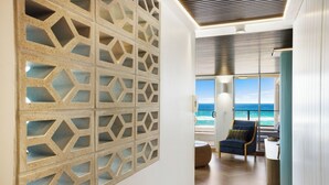 A modern interior with a geometric wall design, a wooden floor, and a view of the ocean.