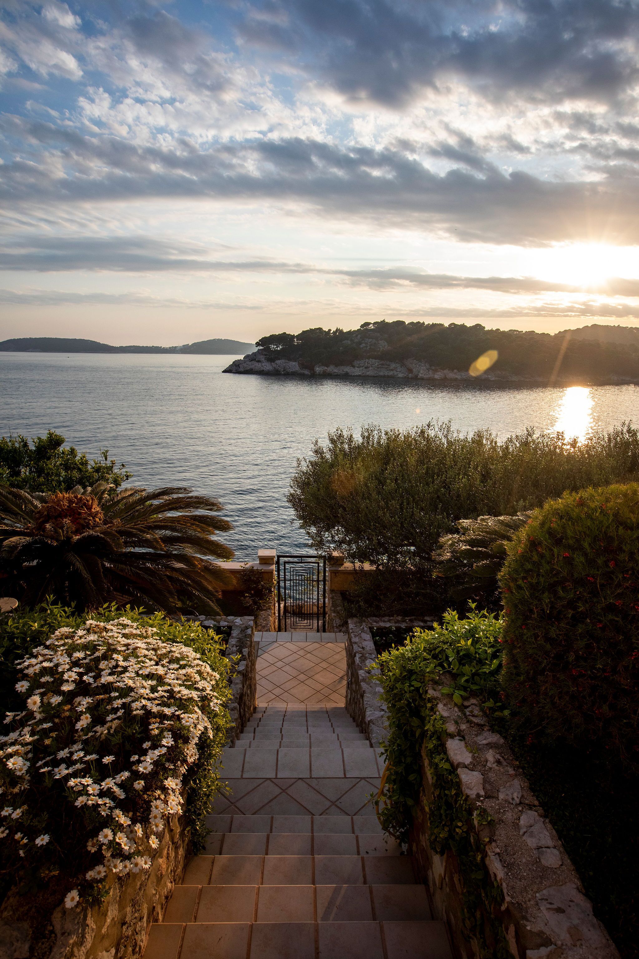 A stone staircase leading to a gate overlooking a body of water with a sunset in the background.