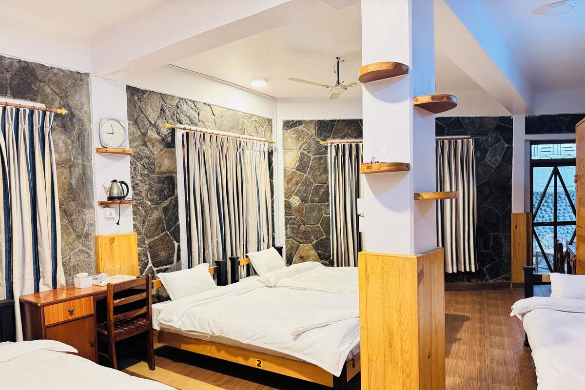 Una habitación de hotel moderna con pared de piedra, una cama con ropa blanca, un escritorio de madera y un pequeño estante con un hervidor.