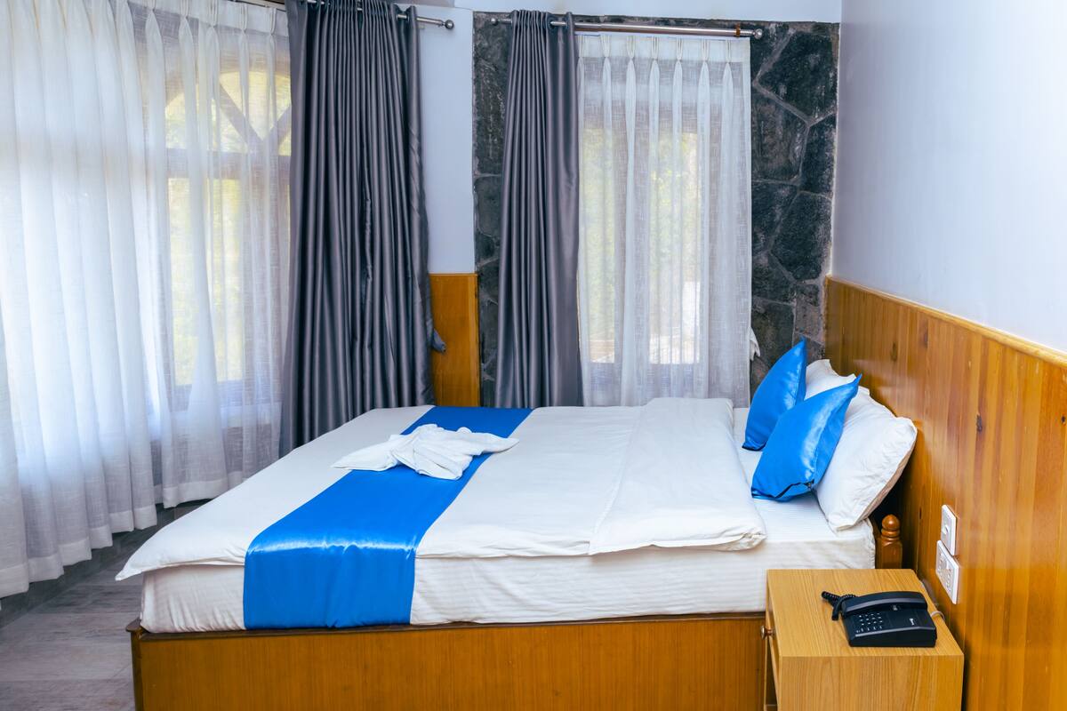 Una cama bien hecha con una colcha azul y blanca, un cabecero de madera y una mesita de noche con un teléfono.