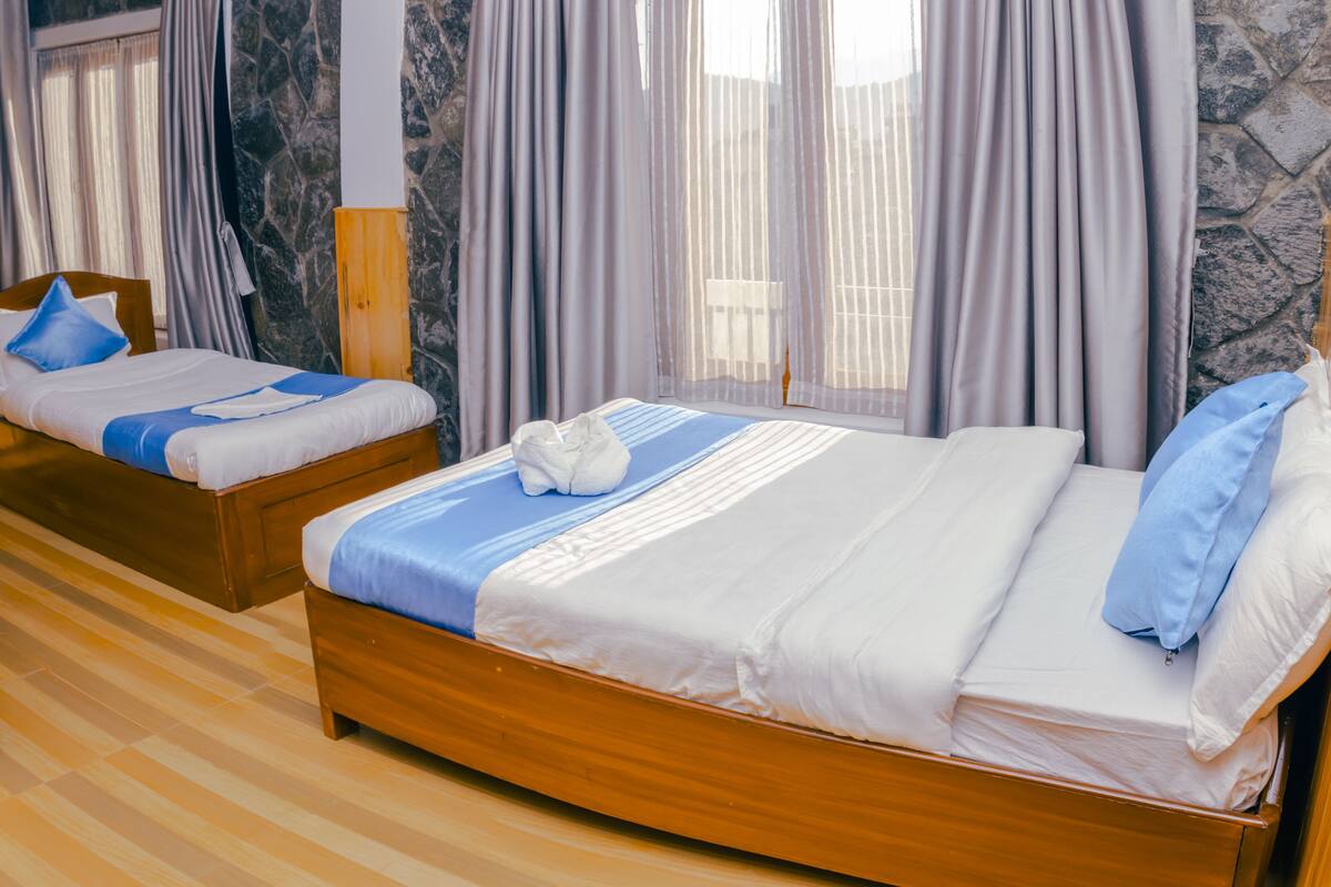 Habitación de hotel con dos camas de madera, una pared de mármol y una ventana con cortinas.