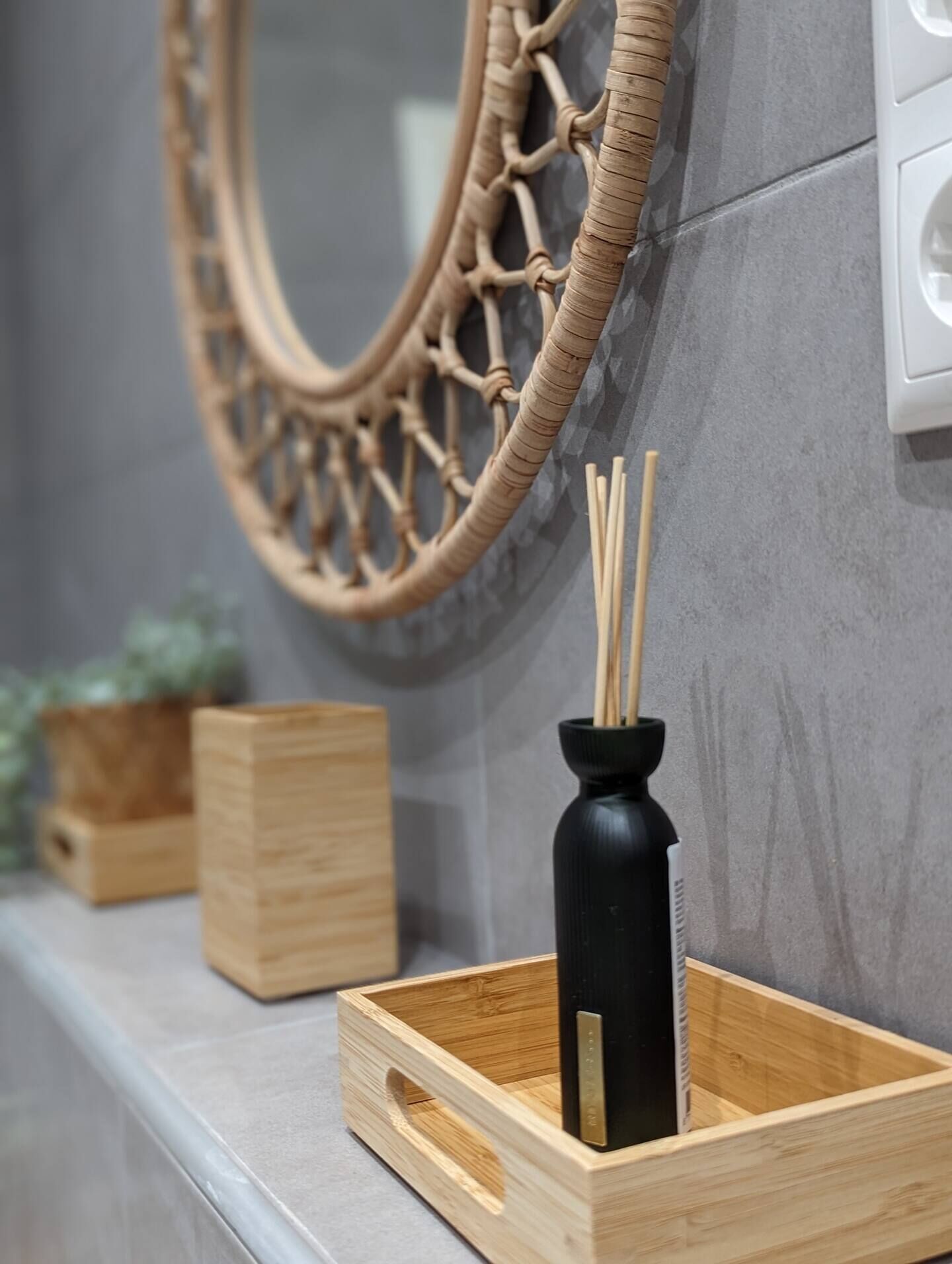 Une salle de bain avec un décor mural en bois, une bouteille noire avec des bâtonnets et des boîtes en bois sur une étagère.
