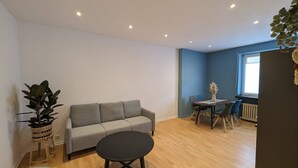 Een moderne woonkamer met een grijze bank, een ronde zwarte salontafel, en een eethoek met een tafel en stoelen.