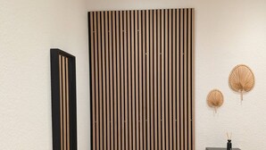 Een modern interieur met een zwarte bank, een verticale houten wandpaneel en een klein zwart plankje met decoratieve objecten.