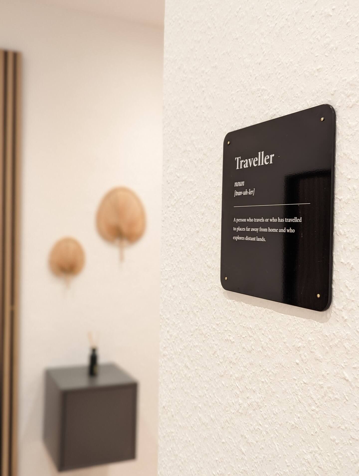 Ein schwarzes Schild an einer weißen Wand mit dem Wort 'Traveller' und einer Definition.