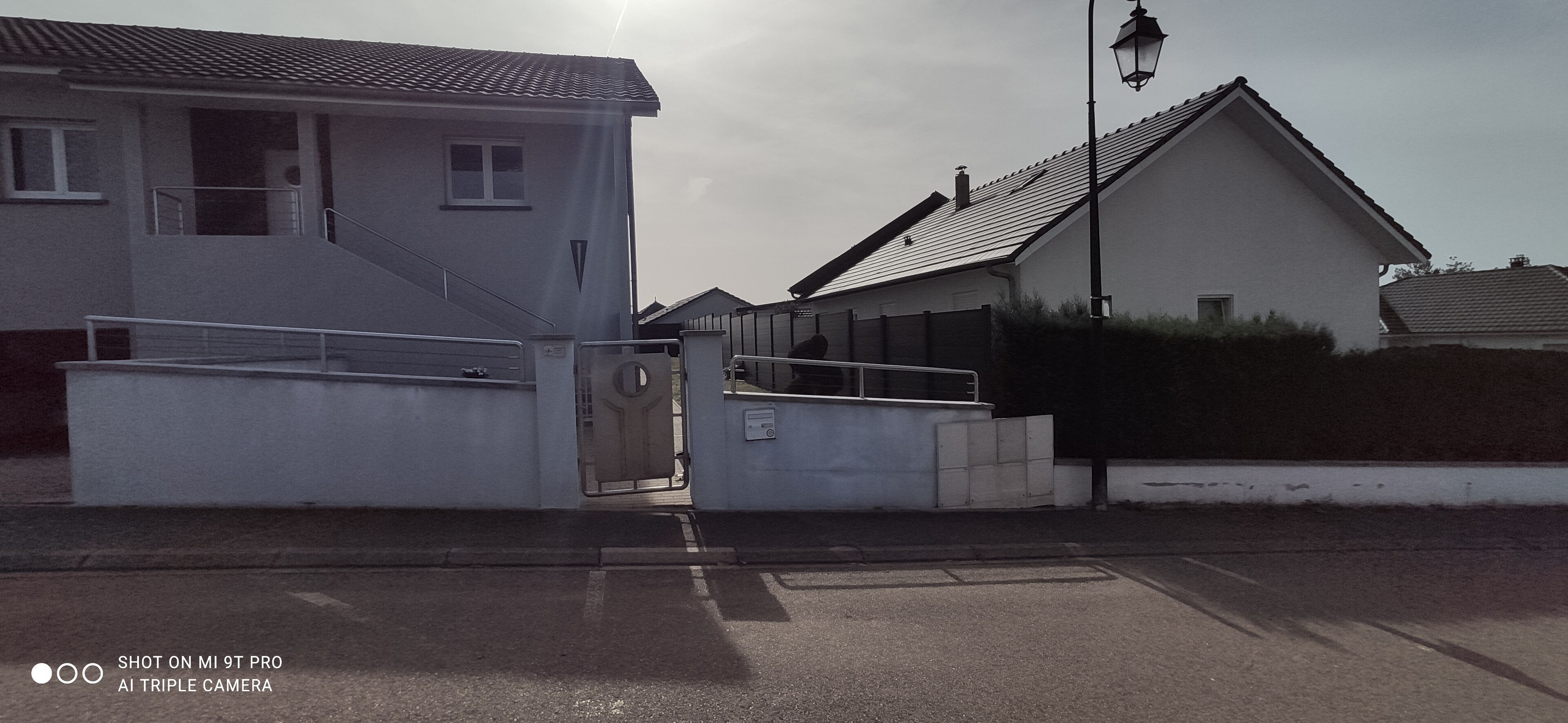 Zona residencial com portão de acesso, escadaria que leva a uma casa e um poste de iluminação.