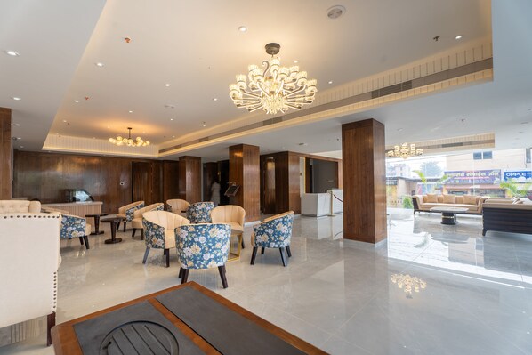 A modern lobby with a chandelier, seating area, and a reception desk. - Hotel De Crown Inn (Tilottama)