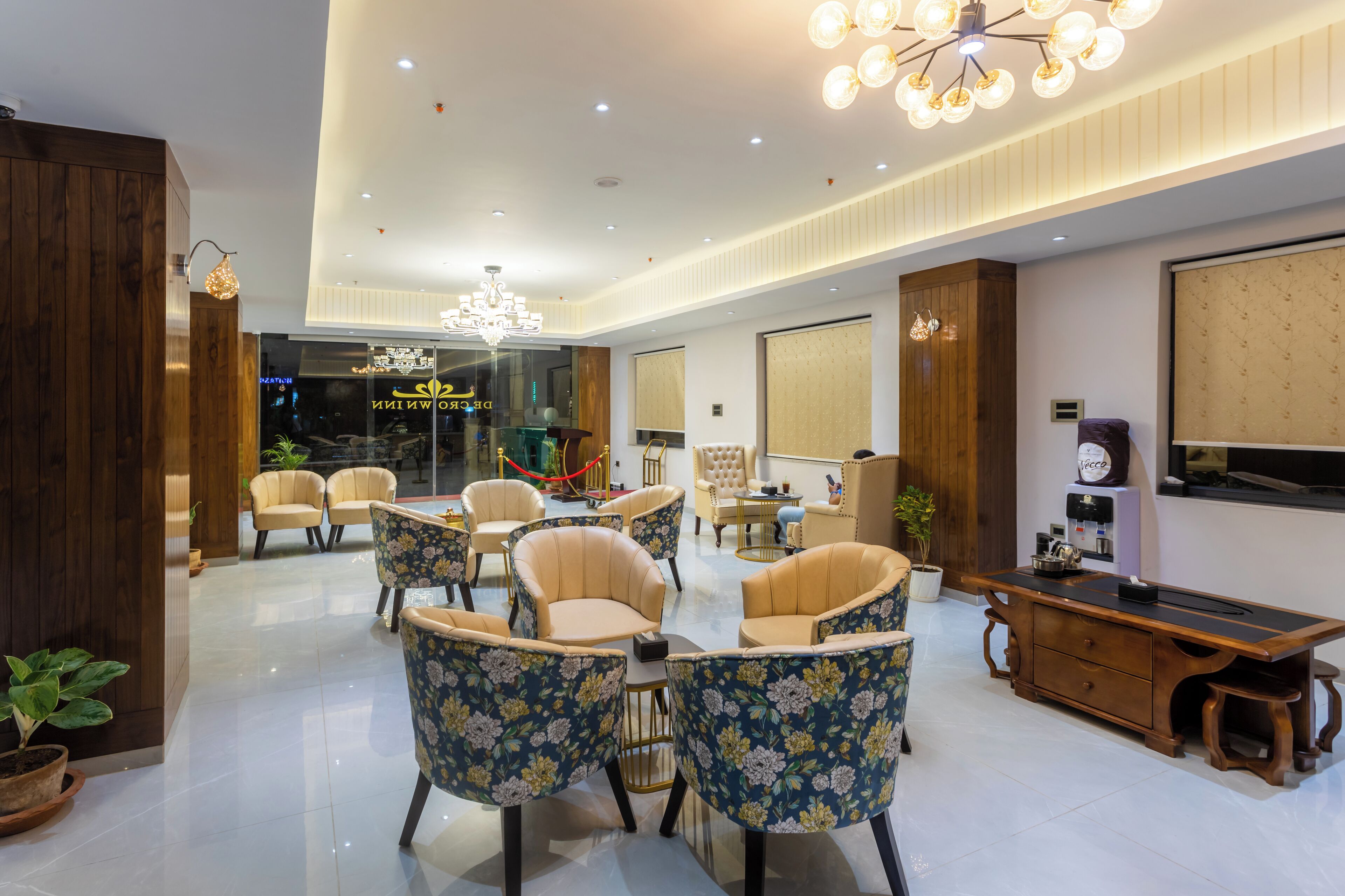 A spacious hotel lobby with modern furniture, a chandelier, and a coffee machine.