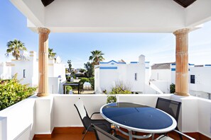 A balcony with a round table and chairs, white walls, and palm trees.