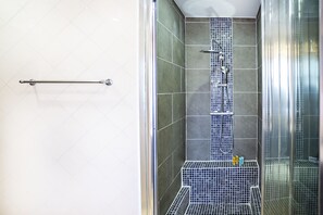 A shower with a glass door, a metal handrail, and a tiled wall.