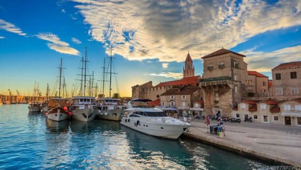 A marina with several yachts docked, a historic building with a tower, and a clear sky.