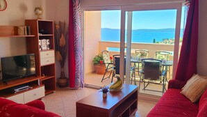 A living room with a television, a bookshelf, a red sofa, and a balcony with a table and chairs.