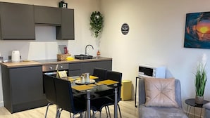 A modern kitchen with dark cabinets, a dining table with chairs, a sofa, and a coffee table.