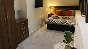 A bedroom with a bed, bedside table, lamp, wardrobe, and a small plant.