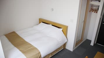 A single bed with a wooden headboard, a white pillow, and a beige blanket. There is a door to the right with a coat rack above it.
