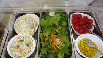 Buffet com diversos pratos, incluindo salada de repolho, salada com cenoura e alface, tomates cereja e milho.