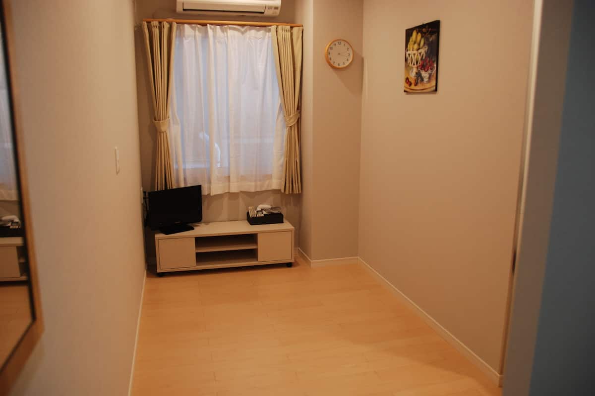 A room with a television on a stand, a clock on the wall, and a painting.