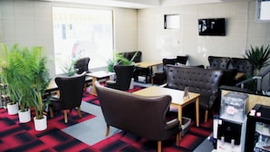 A modern hotel lobby with a check-in counter, seating area with leather chairs, potted plants, and a flat-screen TV on the wall. - Business Hotel Yamate Inn (Kofu)